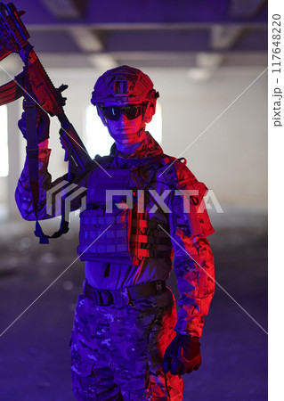 A professional soldier undertakes a perilous mission in an abandoned building illuminated by neon blue and purple lights A professional soldier undertakes a perilous mission in an abandoned building illuminated by neon blue and purple lights 117648220