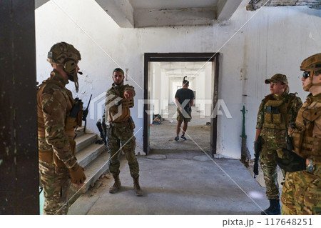 Group of soldiers discusses military tactics while situated in an abandoned building, meticulously planning their moves with focus and determination. 117648251