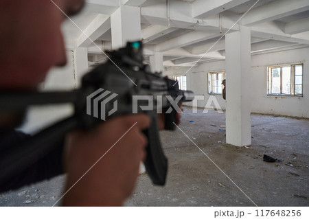 In an abandoned building, a terrorist takes aim with a rifle at a military opponent, engaged in a fierce battle for territorial control, embodying the dangers and tensions of the conflict. 117648256