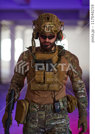 A professional soldier undertakes a perilous mission in an abandoned building illuminated by neon blue and purple lights 117648259