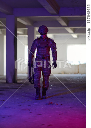 A professional soldier undertakes a perilous mission in an abandoned building illuminated by neon blue and purple lights A professional soldier undertakes a perilous mission in an abandoned building illuminated by neon blue and purple lights 117648486