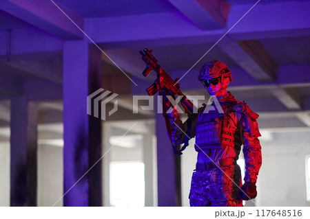 A professional soldier undertakes a perilous mission in an abandoned building illuminated by neon blue and purple lights A professional soldier undertakes a perilous mission in an abandoned building illuminated by neon blue and purple lights 117648516