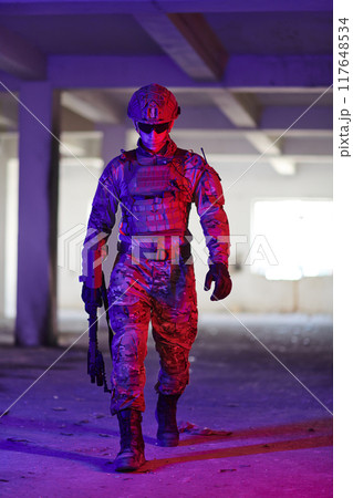 A professional soldier undertakes a perilous mission in an abandoned building illuminated by neon blue and purple lights A professional soldier undertakes a perilous mission in an abandoned building illuminated by neon blue and purple lights 117648534
