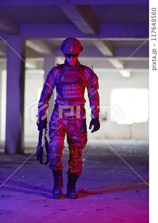 A professional soldier undertakes a perilous mission in an abandoned building illuminated by neon blue and purple lights 117648560