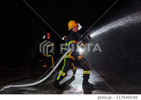 Firefighters using a water hose to eliminate a fire hazard. Team of female and male firemen in dangerous rescue mission.  117648598