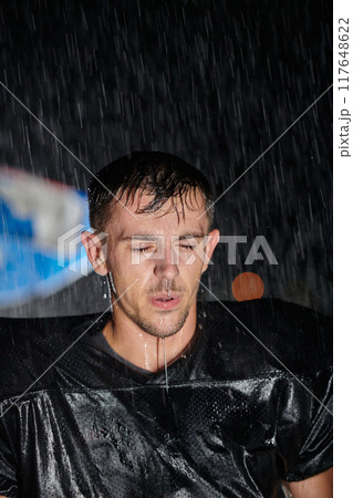 American Football Field: Lonely Athlete Warrior Standing on a Field Holds his Helmet and Ready to Play. Player Preparing to Run, Attack and Score Touchdown. Rainy Night with Dramatic Fog, Blue Light 117648622
