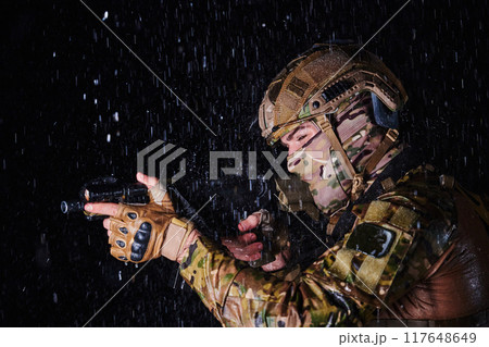 Army soldier in Combat Uniforms with an assault rifle, plate carrier and combat helmet going on a dangerous mission on a rainy night. Army soldier in Combat Uniforms with an assault rifle, plate carrier and combat helmet going on a dangerous mission on a rainy night. 117648649