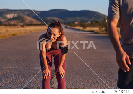 A couple resting after a rigorous morning run, embracing the tranquility of their surroundings as they find rejuvenation, fulfillment, and a deep sense of contentment in each other's company A couple resting after a rigorous morning run, embracing the tranquility of their surroundings as they find rejuvenation, fulfillment, and a deep sense of contentment in each other's company 117648716