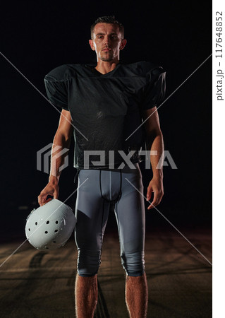 American Football Field: Lonely Athlete Warrior Standing on a Field Holds his Helmet and Ready to Play. Player Preparing to Run, Attack and Score Touchdown. American Football Field: Lonely Athlete Warrior Standing on a Field Holds his Helmet and Ready to Play. Player Preparing to Run, Attack and Score Touchdown. 117648852