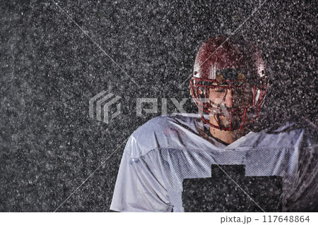 American Football Field: Lonely Athlete Warrior Standing on a Field Holds his Helmet and Ready to Play. Player Preparing to Run, Attack and Score Touchdown. Rainy Night with Dramatic Fog, Blue Light 117648864