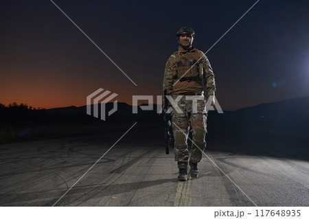 A professional soldier in full military gear striding through the dark night as he embarks on a perilous military mission 117648935