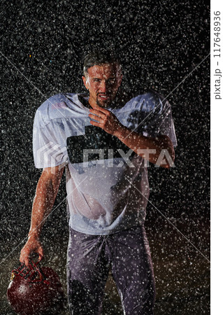 American Football Field: Lonely Athlete Warrior Standing on a Field Holds his Helmet and Ready to Play. Player Preparing to Run, Attack and Score Touchdown. Rainy Night with Dramatic Fog, Blue Light 117648936