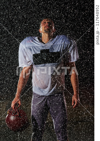 American Football Field: Lonely Athlete Warrior Standing on a Field Holds his Helmet and Ready to Play. Player Preparing to Run, Attack and Score Touchdown. Rainy Night with Dramatic Fog, Blue Light 117648952