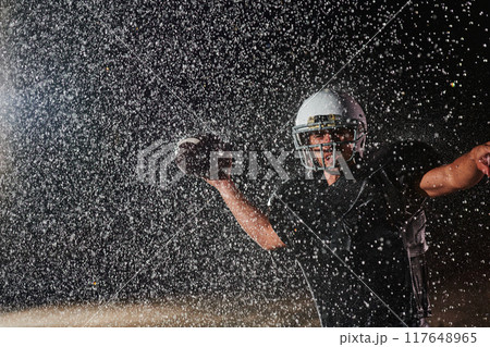 American Football Field: Lonely Athlete Warrior Standing on a Field Holds his Helmet and Ready to Play. Player Preparing to Run, Attack and Score Touchdown. Rainy Night with Dramatic Fog, Blue Light 117648965
