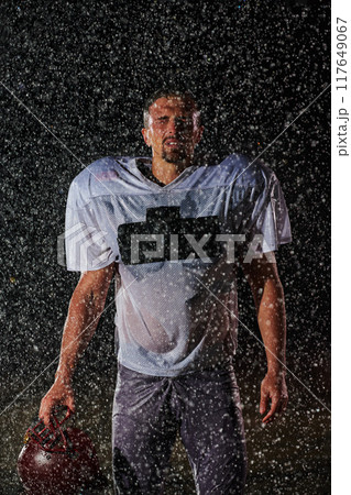 American Football Field: Lonely Athlete Warrior Standing on a Field Holds his Helmet and Ready to Play. Player Preparing to Run, Attack and Score Touchdown. Rainy Night with Dramatic Fog, Blue Light 117649067