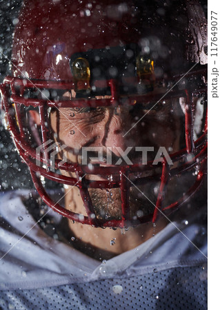 American Football Field: Lonely Athlete Warrior Standing on a Field Holds his Helmet and Ready to Play. Player Preparing to Run, Attack and Score Touchdown. Rainy Night with Dramatic Fog, Blue Light 117649077