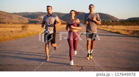 A group of young athletes running together in the early morning light of the sunrise, showcasing their collective energy, determination, and unity  117649078