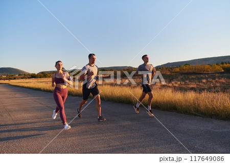 A group of young athletes running together in the early morning light of the sunrise, showcasing their collective energy, determination, and unity A group of young athletes running together in the early morning light of the sunrise, showcasing their collective energy, determination, and unity 117649086