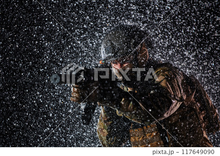 Army soldier in Combat Uniforms with an assault rifle, plate carrier and combat helmet going on a dangerous mission on a rainy night. Army soldier in Combat Uniforms with an assault rifle, plate carrier and combat helmet going on a dangerous mission on a rainy night. 117649090