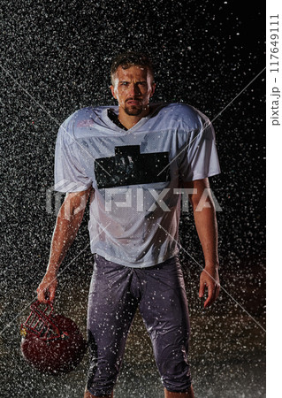 American Football Field: Lonely Athlete Warrior Standing on a Field Holds his Helmet and Ready to Play. Player Preparing to Run, Attack and Score Touchdown. Rainy Night with Dramatic Fog, Blue Light American Football Field: Lonely Athlete Warrior Standing on a Field Holds his Helmet and Ready to Play. Player Preparing to Run, Attack and Score Touchdown. Rainy Night with Dramatic Fog, Blue Light 117649111