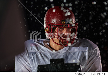 American Football Field: Lonely Athlete Warrior Standing on a Field Holds his Helmet and Ready to Play. Player Preparing to Run, Attack and Score Touchdown. Rainy Night with Dramatic Fog, Blue Light 117649141