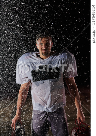 American Football Field: Lonely Athlete Warrior Standing on a Field Holds his Helmet and Ready to Play. Player Preparing to Run, Attack and Score Touchdown. Rainy Night with Dramatic Fog, Blue Light American Football Field: Lonely Athlete Warrior Standing on a Field Holds his Helmet and Ready to Play. Player Preparing to Run, Attack and Score Touchdown. Rainy Night with Dramatic Fog, Blue Light 117649214