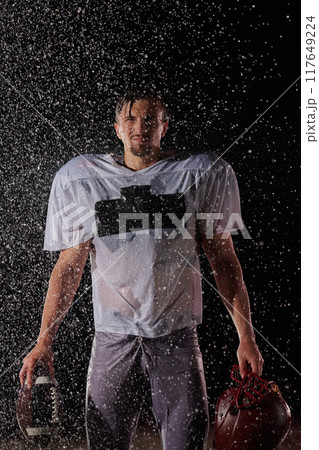 American Football Field: Lonely Athlete Warrior Standing on a Field Holds his Helmet and Ready to Play. Player Preparing to Run, Attack and Score Touchdown. Rainy Night with Dramatic Fog, Blue Light American Football Field: Lonely Athlete Warrior Standing on a Field Holds his Helmet and Ready to Play. Player Preparing to Run, Attack and Score Touchdown. Rainy Night with Dramatic Fog, Blue Light 117649224
