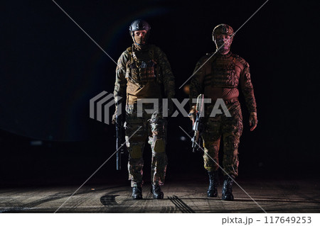 Two professional soldiers marching through the dark of night on a dangerous mission, epitomizing their unwavering bravery, unwavering teamwork, and the high-stakes intensity of their specialized 117649253