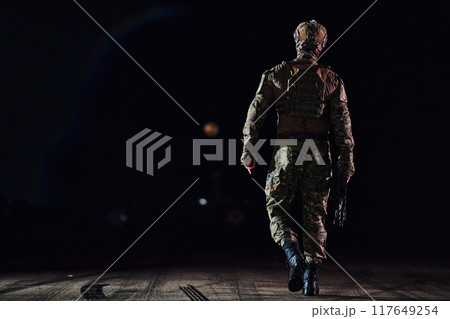 A professional soldier in full military gear striding through the dark night as he embarks on a perilous military mission 117649254