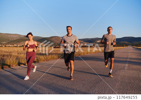 A group of young athletes running together in the early morning light of the sunrise, showcasing their collective energy, determination, and unity  117649255