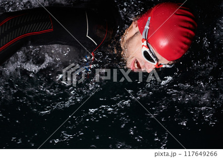 A determined professional triathlete undergoes rigorous night time training in cold waters, showcasing dedication and resilience in preparation for an upcoming triathlon swim competition 117649266