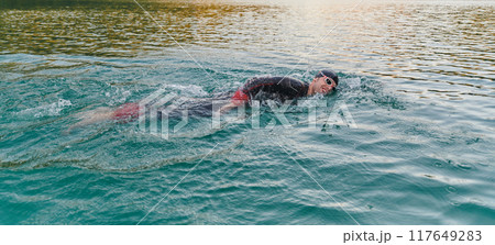 A professional triathlete trains with unwavering dedication for an upcoming competition at a lake, emanating a sense of athleticism and profound commitment to excellence. A professional triathlete trains with unwavering dedication for an upcoming competition at a lake, emanating a sense of athleticism and profound commitment to excellence. 117649283