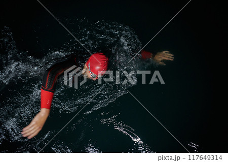 A determined professional triathlete undergoes rigorous night time training in cold waters, showcasing dedication and resilience in preparation for an upcoming triathlon swim competition A determined professional triathlete undergoes rigorous night time training in cold waters, showcasing dedication and resilience in preparation for an upcoming triathlon swim competition 117649314