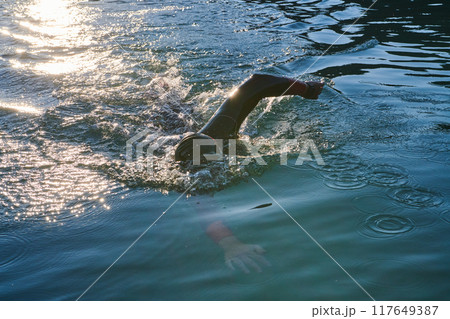Triathlon athlete swimming on lake in sunrise wearing wetsuit 117649387