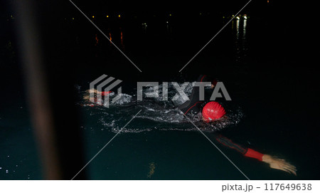 A determined professional triathlete undergoes rigorous night time training in cold waters, showcasing dedication and resilience in preparation for an upcoming triathlon swim competition A determined professional triathlete undergoes rigorous night time training in cold waters, showcasing dedication and resilience in preparation for an upcoming triathlon swim competition 117649638