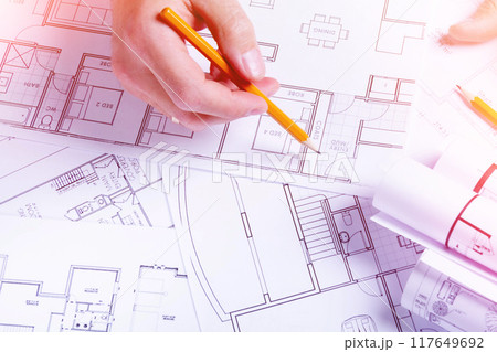 Builder's hands on the background of a house plan. Construction planning. Drawing up an estimate. Builder's hands on the background of a house plan. Construction planning. Drawing up an estimate. 117649692
