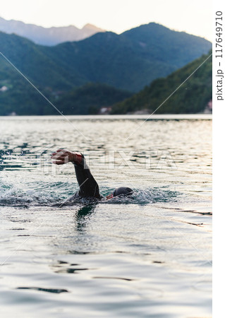 A professional triathlete trains with unwavering dedication for an upcoming competition at a lake, emanating a sense of athleticism and profound commitment to excellence. 117649710