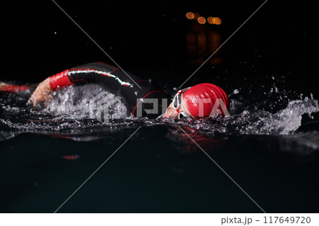 A determined professional triathlete undergoes rigorous night time training in cold waters, showcasing dedication and resilience in preparation for an upcoming triathlon swim competition 117649720