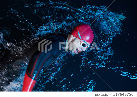 A determined professional triathlete undergoes rigorous night time training in cold waters, showcasing dedication and resilience in preparation for an upcoming triathlon swim competition 117649750