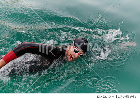 A professional triathlete trains with unwavering dedication for an upcoming competition at a lake, emanating a sense of athleticism and profound commitment to excellence. 117649945