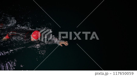 A determined professional triathlete undergoes rigorous night time training in cold waters, showcasing dedication and resilience in preparation for an upcoming triathlon swim competition A determined professional triathlete undergoes rigorous night time training in cold waters, showcasing dedication and resilience in preparation for an upcoming triathlon swim competition 117650059