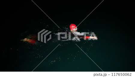 A determined professional triathlete undergoes rigorous night time training in cold waters, showcasing dedication and resilience in preparation for an upcoming triathlon swim competition A determined professional triathlete undergoes rigorous night time training in cold waters, showcasing dedication and resilience in preparation for an upcoming triathlon swim competition 117650062