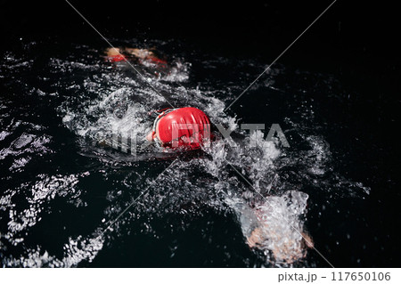 A determined professional triathlete undergoes rigorous night time training in cold waters, showcasing dedication and resilience in preparation for an upcoming triathlon swim competition A determined professional triathlete undergoes rigorous night time training in cold waters, showcasing dedication and resilience in preparation for an upcoming triathlon swim competition 117650106