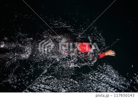 A determined professional triathlete undergoes rigorous night time training in cold waters, showcasing dedication and resilience in preparation for an upcoming triathlon swim competition 117650143
