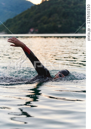 A professional triathlete trains with unwavering dedication for an upcoming competition at a lake, emanating a sense of athleticism and profound commitment to excellence. 117650150