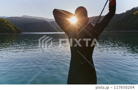 Authentic triathlon athlete getting ready for swimming training on lake Authentic triathlon athlete getting ready for swimming training on lake 117650204