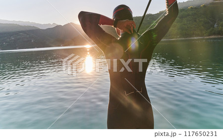 Authentic triathlon athlete getting ready for swimming training on lake Authentic triathlon athlete getting ready for swimming training on lake 117650231