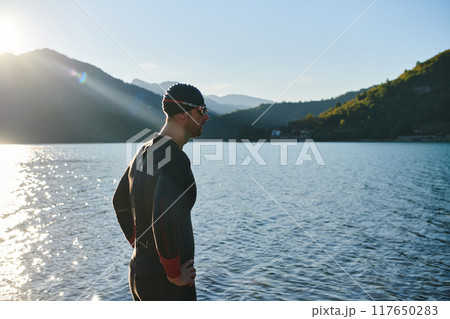 Authentic triathlon athlete getting ready for swimming training on lake Authentic triathlon athlete getting ready for swimming training on lake 117650283
