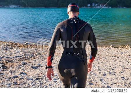 Authentic triathlon athlete getting ready for swimming training on lake Authentic triathlon athlete getting ready for swimming training on lake 117650375