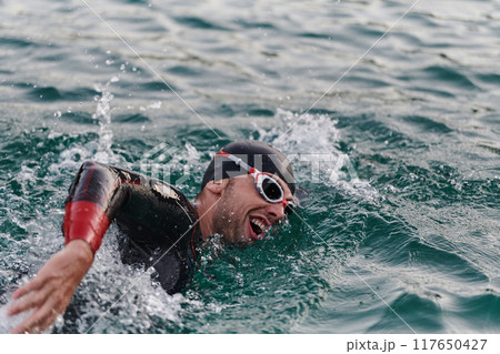 A professional triathlete trains with unwavering dedication for an upcoming competition at a lake, emanating a sense of athleticism and profound commitment to excellence. 117650427